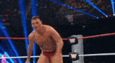 a shirtless wrestler in a wrestling ring with the letter w on the ropes .