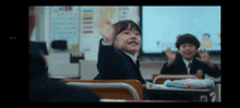 a little girl is raising her hand in a classroom while sitting at a desk .