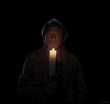 a man in a trench coat holds a lit candle in front of his mouth