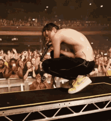 a man without a shirt is singing into a microphone on a stage in front of a crowd