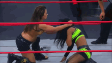 two women are wrestling in a ring and one of them is wearing a neon green top with the letter m on it