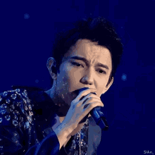 a man is singing into a microphone while wearing a purple jacket .