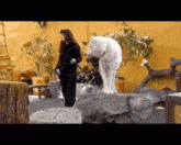 a woman is standing next to a white wolf standing on a rock