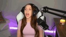 a woman wearing headphones and a pink shirt sitting in front of a microphone