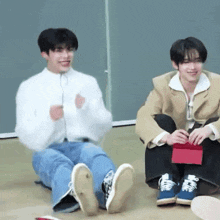 two young men are sitting on the floor with their legs crossed and laughing .