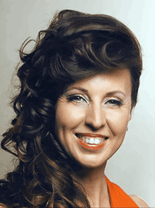 a woman with long curly hair is smiling and wearing red lipstick