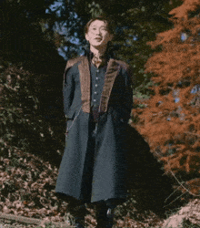 a man in a long coat is standing in the woods pointing