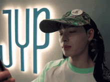 a young man wearing a hat and a bandana stands in front of a jup sign