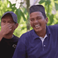 a man in a blue shirt is laughing while covering his mouth with his hand