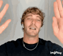 a man wearing headphones and a necklace is making a funny face with his hands in the air ..