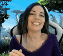 a woman in a purple shirt is smiling in front of a landscape with trees and mountains