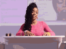a woman in a pink shirt is sitting at a podium with the word sunday on the screen behind her
