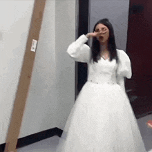 a woman in a white wedding dress is standing in a hallway covering her face .