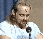 a man with a cross painted on his forehead is talking into a microphone