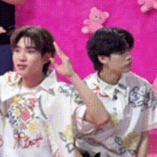 two men are standing next to each other in front of a pink wall with teddy bears on it .
