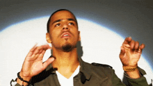 a man in a green jacket and white shirt is looking up with his arms outstretched