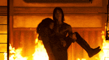 a man is holding a woman in his arms in front of a fire
