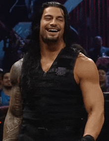 a man with long hair and a beard is smiling and wearing a black vest .