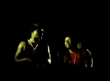 a man in a black tank top is blowing a flame out of his mouth in a dark room .