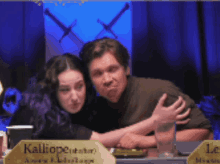 a man and a woman are hugging in front of a sign that says kalliopei