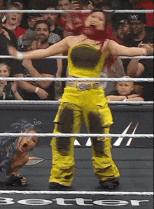 a woman in yellow pants is standing in a wrestling ring with the word better on the bottom