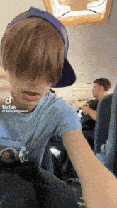 a young man wearing a blue shirt and a purple hat has a tiktok sticker on his face