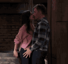 a man and a woman kissing in front of a brick wall