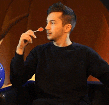 a young man in a black sweater is eating a lollipop