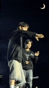 a man in a black hoodie stands next to another man in blue jeans