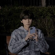 a man in a plaid shirt is sitting in a chair holding a cell phone in his hand