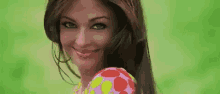 a woman with long hair is smiling and holding a pink and yellow polka dot ball .