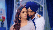 a man in a blue turban is hugging a woman in a white dress