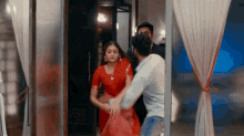 a woman in a red saree is standing next to a man in a white shirt in a room .