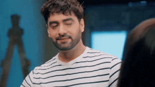 a man with a beard wearing a striped shirt is smiling while looking at a woman .
