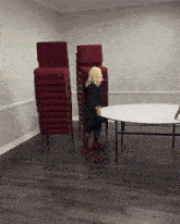 a woman stands in front of a table with a stack of red chairs