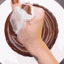 a person is spreading chocolate on a cake with a piece of wax paper