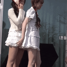 two women standing next to each other with one wearing a red hat and the other wearing a white skirt