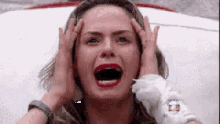 a woman is screaming and holding her head with her hands .