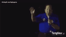 a man in a blue shirt is holding a microphone and talking into it .