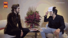 two men are sitting at a table with flowers and a sign that says premio multi show 2016