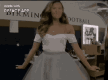 a woman in a white off the shoulder top and a blue skirt is dancing in front of a sign that says birming football