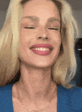 a blonde woman wearing a blue shirt and a gold chain smiles