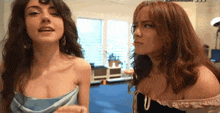 two women are standing next to each other in a room and one of them is looking at the camera .