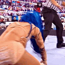 a woman with blue hair is kneeling down in a wrestling ring while a referee looks on