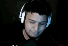 a man wearing headphones is smiling in front of a microphone in a dark room .