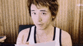a man in a tank top is holding a piece of paper and making a funny face .