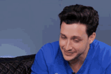 a man in a blue scrub top is sitting on a couch making a funny face .
