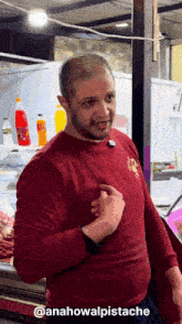 a man in a red shirt is standing in front of a fridge with bottles of orange soda on it