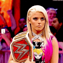 a blonde woman with pink hair is holding a wrestling championship belt in front of a crowd .
