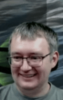 a man wearing glasses and a gray shirt is smiling for the camera .